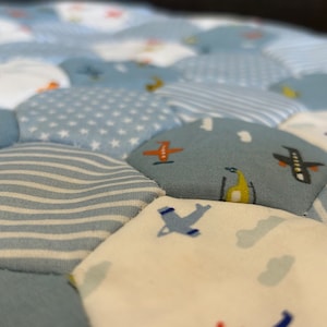 May include: A blue and white baby play mat with a hexagonal pattern. Each hexagon features a different design, including aeroplanes, stars, and stripes.
