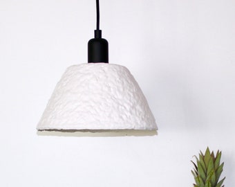 May include: A white, textured, paper lampshade hangs from a black cord.  Three yellow lemons and a green apple sit on a teal blue table with a pineapple beside them.