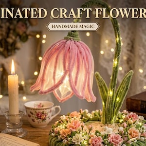 Könnte beinhalten: Beleuchtete Bastelblumenlampe mit rosafarbenem blütenförmigem Schirm und grünem Stiel. Der Sockel ist mit kleinen Blumen verziert. Die Lampe steht auf einem Holztisch mit einer brennenden Kerze und einer Teetasse.