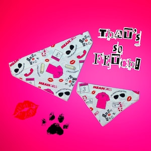 May include: Two white triangle-shaped dog bandanas with a Mean Girls theme. The bandanas feature a pink and white print with images of sunglasses, lips, candy canes, and the text "Mean Girls" and "Burn Book". The bandanas are on a pink background with a black paw print and a red lip print.
