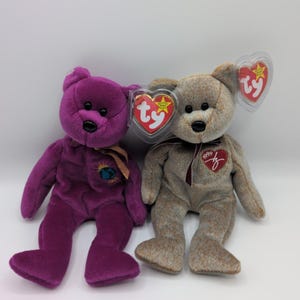 Puede incluir: Dos osos de peluche Beanie Baby. Uno es morado con una cinta dorada y un pequeño parche. El otro es marrón con una etiqueta roja en forma de corazón y una cinta roja. Ambos tienen ojos y narices negros.
