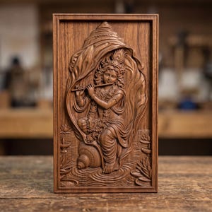 May include: A rectangular wooden wall plaque featuring a detailed relief carving of a figure playing a flute. The central figure is framed by a large conch shell design, with lotus flowers and small oil lamps carved into the lower corners.