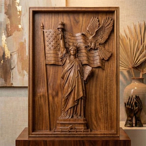 May include: A rectangular wooden wall plaque featuring a detailed relief carving of the Statue of Liberty holding a torch and tablet, positioned in front of an American flag with a large eagle in flight above, all framed in a dark wood border.