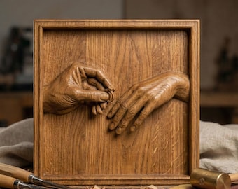 May include: A wooden relief carving of two hands, one placing a ring on the other. The artwork is framed within a square wooden panel, showcasing detailed craftsmanship and a warm, natural wood tone. The carving is set on a wooden surface.