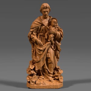 Puede incluir: Estatua de madera que representa a un hombre con barba sosteniendo a un niño. El hombre viste túnicas drapeadas, y el niño también está envuelto en tela. La estatua, tallada en madera clara, se apoya en una base con follaje tallado.