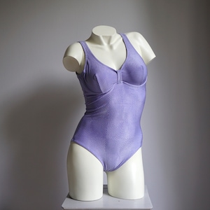 May include: A purple swimsuit with a swirling pattern. The swimsuit has a scoop neck and a built-in bra.