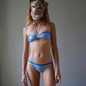 May include: A woman wearing a blue and white striped bikini top and matching bikini bottoms. She is wearing a lion mask over her face.
