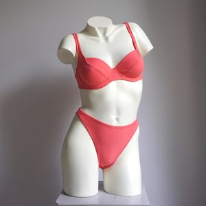May include: Coral-colored bikini set displayed on a white mannequin. The set includes a structured underwire bra with adjustable straps and a high-cut bikini bottom. The mannequin is positioned against a plain gray background.