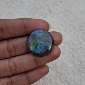 May include: A round, polished labradorite gemstone with iridescent blue, green, and gold hues. The stone is set against a neutral background, showcasing its natural colors and patterns. This gemstone is ideal for jewelry making or collecting.