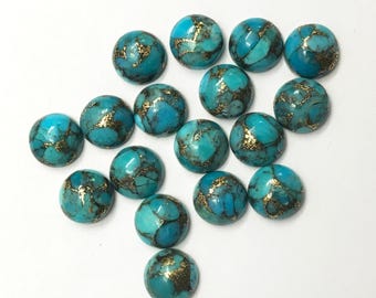 May include: A collection of round, turquoise-colored gemstones with gold-colored veining. The stones are arranged on a white surface, showcasing their polished, domed surfaces. The gemstones are likely used for jewelry making or crafting.