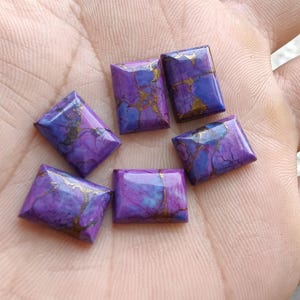 May include: Five rectangular cabochons featuring a polished purple and blue surface with distinct gold-colored veining patterns. Each stone has a smooth, flat base and a slightly domed top, showcasing a vibrant marbled appearance throughout.