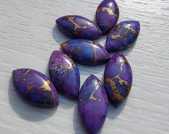 May include: A collection of oval-shaped gemstones in shades of purple and blue, with gold-colored veining. The gemstones are arranged on a light-colored surface, showcasing their polished, glossy finish. These stones could be used for jewelry making.