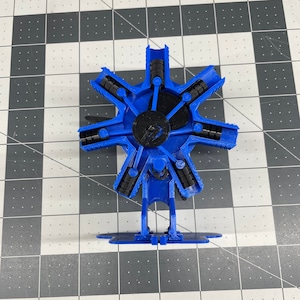 Op de afbeelding: Een blauw 3D-geprint model van een zescilindermotor met een zwarte basis. De motor heeft een stervormig ontwerp met zes cilinders die rond een centrale naaf zijn gerangschikt.