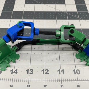 May include: A 3D printed robotic arm with two joints, one blue and one green, connected by a black rod. The arm is mounted on a green base.
