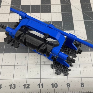May include: A 3D printed blue and black model of a small vehicle with a rotating drum. The vehicle has a long, thin arm extending from the side.