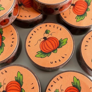 Peut inclure: Un ensemble de six rouleaux de ruban washi avec un motif de champ de citrouilles. Le ruban est orange avec des feuilles vertes et des tiges brunes. Le texte sur le ruban est "Pumpkin Patch Washi".