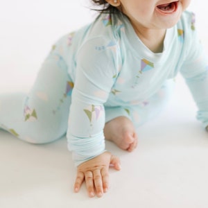 K&ouml;nnte beinhalten: Ein Baby tr&auml;gt einen hellblauen lang&auml;rmeligen Schlafanzug mit einem bunten Drachenmuster. Der Schlafanzug hat einen Rundhalsausschnitt und lange Hosen.