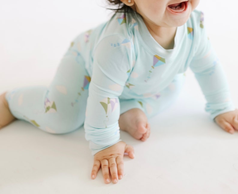 K&ouml;nnte beinhalten: Ein Baby tr&auml;gt einen hellblauen lang&auml;rmeligen Schlafanzug mit einem bunten Drachenmuster. Der Schlafanzug hat einen Rundhalsausschnitt und lange Hosen.