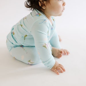 K&ouml;nnte beinhalten: Ein Baby tr&auml;gt einen hellblauen lang&auml;rmeligen Schlafanzug mit einem bunten Drachenmuster. Der Schlafanzug ist aus weichem, bequemem Stoff.