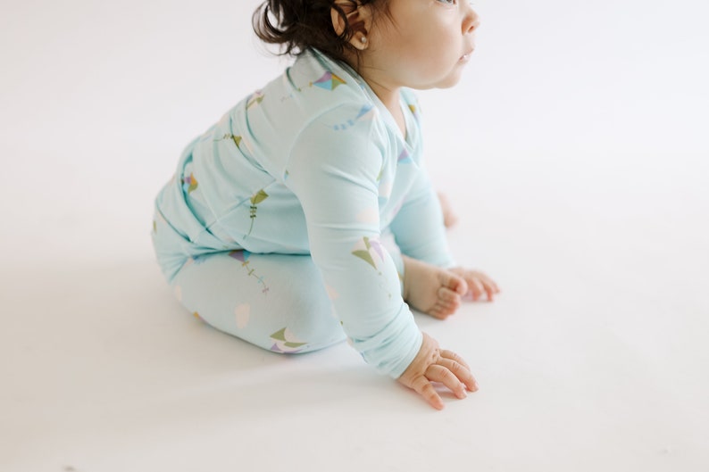 K&ouml;nnte beinhalten: Ein Baby tr&auml;gt einen hellblauen lang&auml;rmeligen Schlafanzug mit einem bunten Drachenmuster. Der Schlafanzug ist aus weichem, bequemem Stoff.