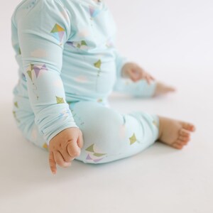 K&ouml;nnte beinhalten: Ein Baby tr&auml;gt einen hellblauen lang&auml;rmeligen Schlafanzug mit einem Drachenmuster. Der Schlafanzug hat ein wei&szlig;es Wolken- und buntes Drachenmuster.