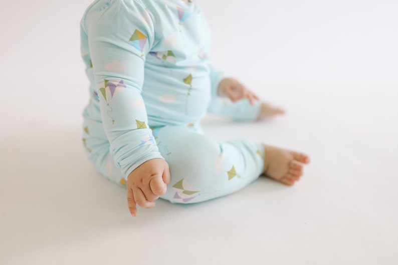 K&ouml;nnte beinhalten: Ein Baby tr&auml;gt einen hellblauen lang&auml;rmeligen Schlafanzug mit einem Drachenmuster. Der Schlafanzug hat ein wei&szlig;es Wolken- und buntes Drachenmuster.