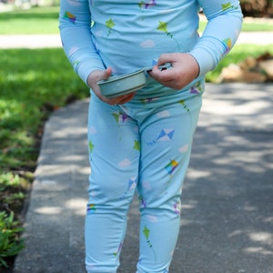 K&ouml;nnte beinhalten: Ein Kind tr&auml;gt einen hellblauen Schlafanzug mit einem Drachenmuster. Der Schlafanzug hat lange &Auml;rmel und lange Hosen. Das Kind h&auml;lt einen kleinen, hellblauen Beh&auml;lter.