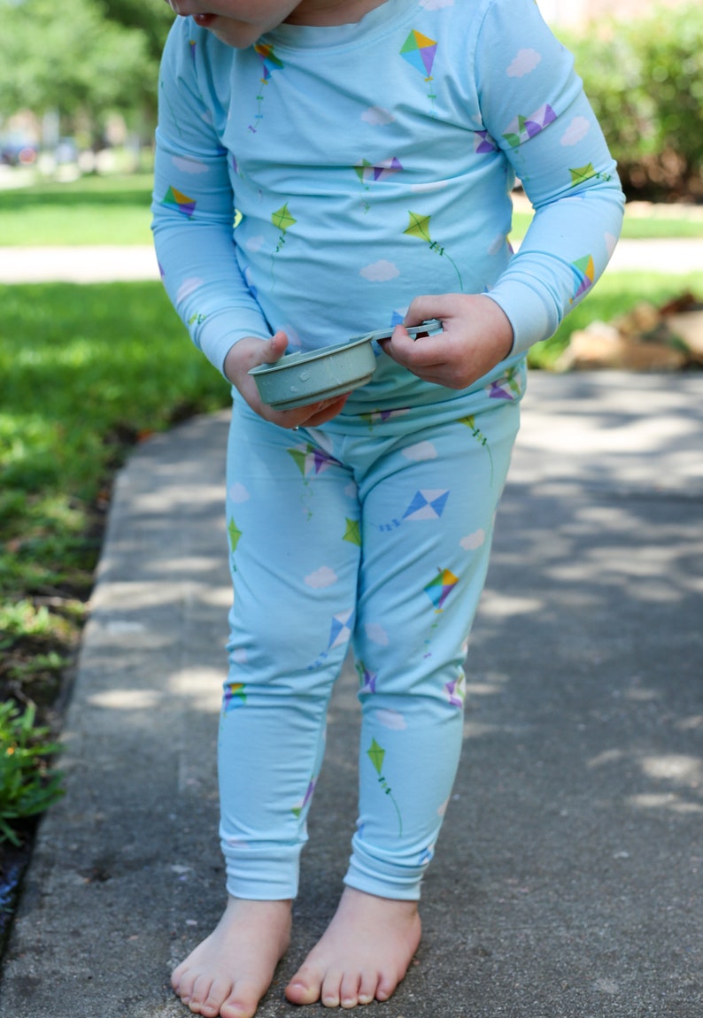 K&ouml;nnte beinhalten: Ein Kind tr&auml;gt einen hellblauen Schlafanzug mit einem Drachenmuster. Der Schlafanzug hat lange &Auml;rmel und lange Hosen. Das Kind h&auml;lt einen kleinen, hellblauen Beh&auml;lter.