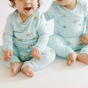 K&ouml;nnte beinhalten: Zwei Babys tragen passende hellblaue Pyjamas mit einem bunten Drachenmuster. Die Pyjamas haben lange &Auml;rmel und lange Hosen.