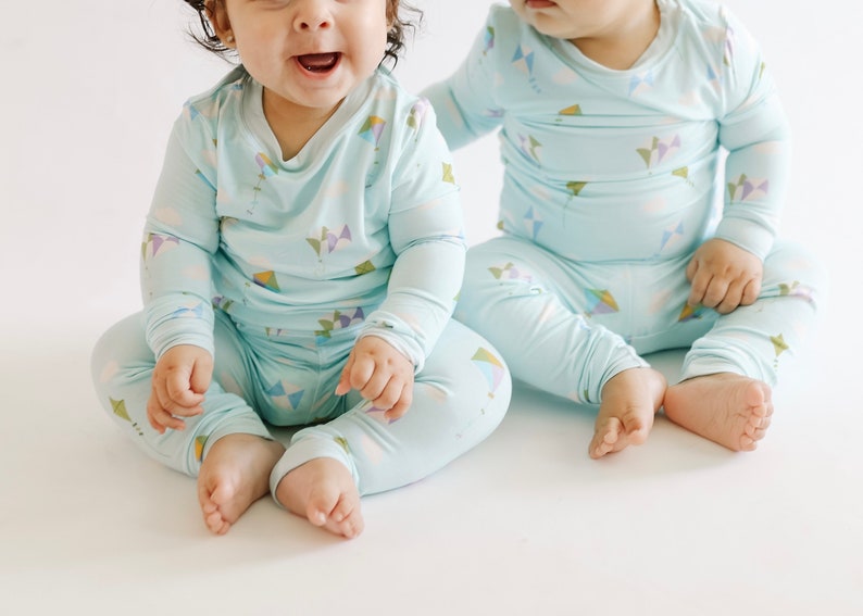 K&ouml;nnte beinhalten: Zwei Babys tragen passende hellblaue Pyjamas mit einem bunten Drachenmuster. Die Pyjamas haben lange &Auml;rmel und lange Hosen.