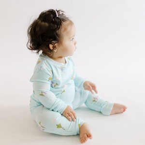 K&ouml;nnte beinhalten: Ein Baby tr&auml;gt einen hellblauen lang&auml;rmeligen Schlafanzug mit einem Drachenmuster. Der Schlafanzug hat einen Rundhalsausschnitt und lange Hosen.