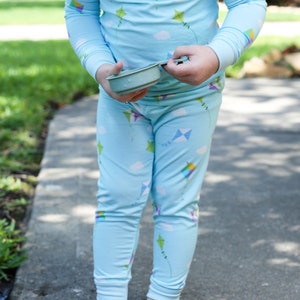 K&ouml;nnte beinhalten: Ein Kind tr&auml;gt einen blauen Schlafanzug mit einem Drachenmuster. Der Schlafanzug hat lange &Auml;rmel und lange Hosen. Das Kind h&auml;lt einen kleinen, hellblauen Beh&auml;lter.