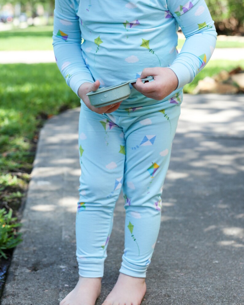 K&ouml;nnte beinhalten: Ein Kind tr&auml;gt einen blauen Schlafanzug mit einem Drachenmuster. Der Schlafanzug hat lange &Auml;rmel und lange Hosen. Das Kind h&auml;lt einen kleinen, hellblauen Beh&auml;lter.