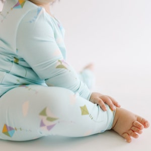 K&ouml;nnte beinhalten: Ein Baby tr&auml;gt einen hellblauen lang&auml;rmeligen Schlafanzug mit einem bunten Drachenmuster. Der Schlafanzug hat eine lockere Passform und ist aus einem weichen, bequemen Stoff gefertigt.