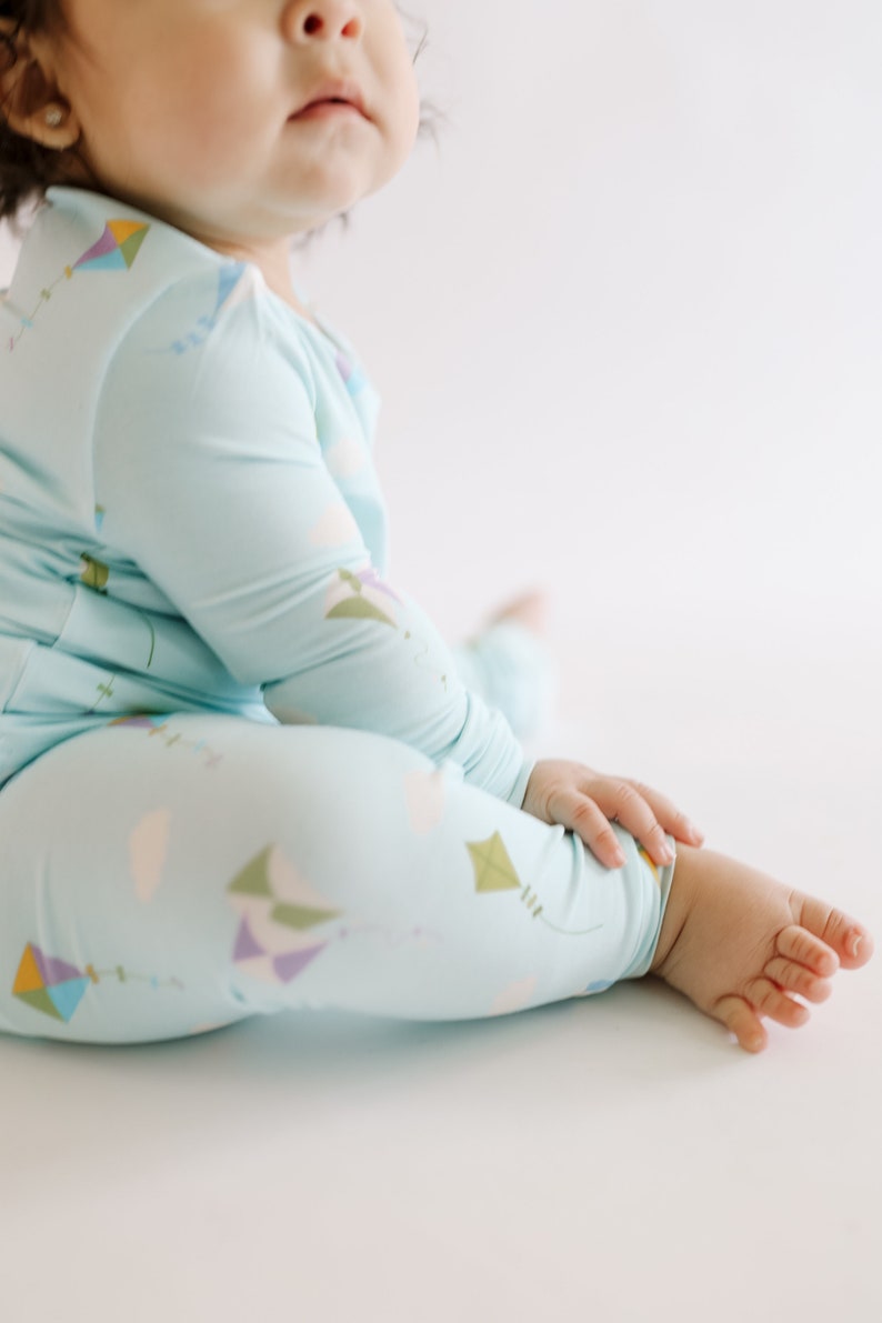 K&ouml;nnte beinhalten: Ein Baby tr&auml;gt einen hellblauen lang&auml;rmeligen Schlafanzug mit einem bunten Drachenmuster. Der Schlafanzug hat eine lockere Passform und ist aus einem weichen, bequemen Stoff gefertigt.