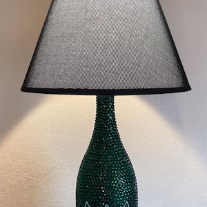May include: A green glass bottle lamp with a black lampshade. The bottle is covered in rhinestones and has the label "Champagne Dom Perignon Vintage Brut" on it.