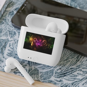 Puede incluir: Auriculares inalámbricos blancos en una caja de carga con una pequeña pantalla que muestra una imagen colorida de un mando de videojuego.