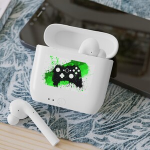 Puede incluir: Auriculares inalámbricos blancos en un estuche de carga con un gráfico de mando de videojuego verde y negro.