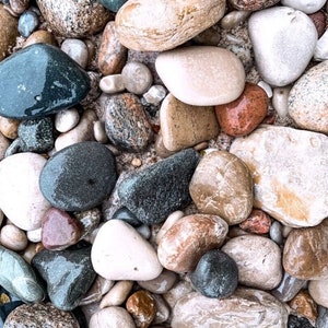 May include: A collection of smooth, colorful river rocks in various shades of gray, brown, white, and red. The rocks are arranged in a random pattern, creating a natural and organic texture.