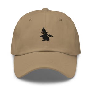 Peut inclure: Casquette de baseball beige avec une visière incurvée. La casquette présente une silhouette noire brodée d'une sorcière sur le devant. Le chapeau a un design classique à six panneaux avec une sangle en tissu et une fermeture à boucle métallique.