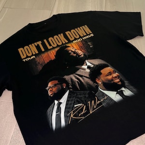 May include: A black short-sleeve t-shirt featuring a graphic print of Rod Wave in a plaid suit. The text reads DON'T LOOK DOWN TOUR and ROD WAVE in gold lettering. A signature in gold script is positioned over the lower right portion of the graphic.