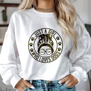 May include: White sweatshirt with a black graphic design of a woman with a bun and glasses. The graphic says "Just a girl who loves dogs" with paw prints around the text.