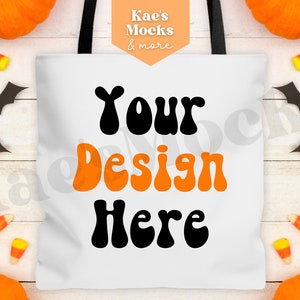 May include: White tote bag with black handles and the text "Your Design Here" in orange and black retro font. The bag is surrounded by pumpkins, candy corn, and bats.