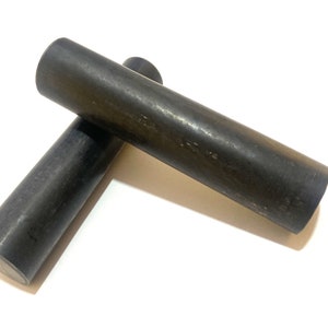 Op de afbeelding: Twee zwarte cilindrische staven, mogelijk gemaakt van hout of plastic, liggen op een wit oppervlak. De staven zijn ongeveer 25 cm lang en 2,5 cm in diameter.