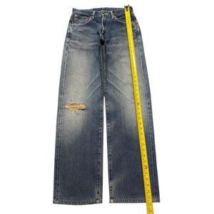 May include: Blue denim jeans with a faded wash, a button fly, and a distressed tear on the right thigh. A yellow measuring tape is placed along the side, showing a total length of approximately 43 inches from the waistband to the hem.