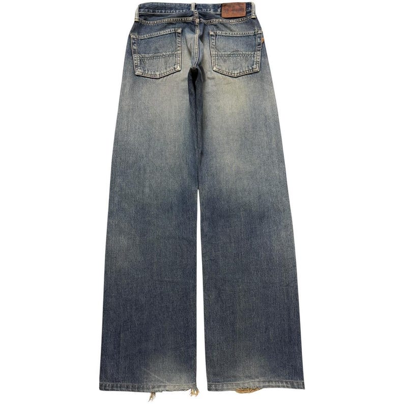 May include: A pair of wide-leg blue denim jeans featuring a faded wash, two back pockets with reinforced stitching, a brown leather patch on the waistband, and frayed hems at the bottom of the legs. The jeans have a classic five-pocket construction.