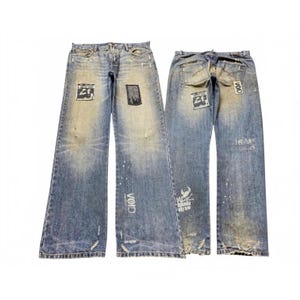 May include: Two pairs of light blue denim jeans with a distressed finish. The jeans feature various black and white patches, white paint splatters, and printed text including the word VOID and the phrase I NEVER. The hems show frayed edges.