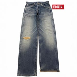 May include: Blue denim jeans by EDWIN featuring a faded wash, a straight-leg silhouette, and a distressed rip on the right thigh. The jeans include a button fly, belt loops, and classic five-pocket styling with visible whiskering and fading.
