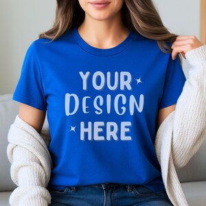 May include: A royal blue t-shirt with the text "YOUR DESIGN HERE" in white, with star accents. The shirt is short-sleeved and has a crew neck. A cream-colored cardigan is draped over the shoulders.