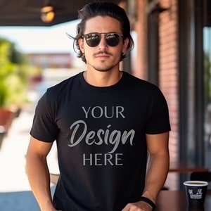 Op de afbeelding: Een man draagt een zwart T-shirt met de tekst "YOUR Design HERE" erop gedrukt. Hij draagt een zonnebril en staat voor een bakstenen gebouw.